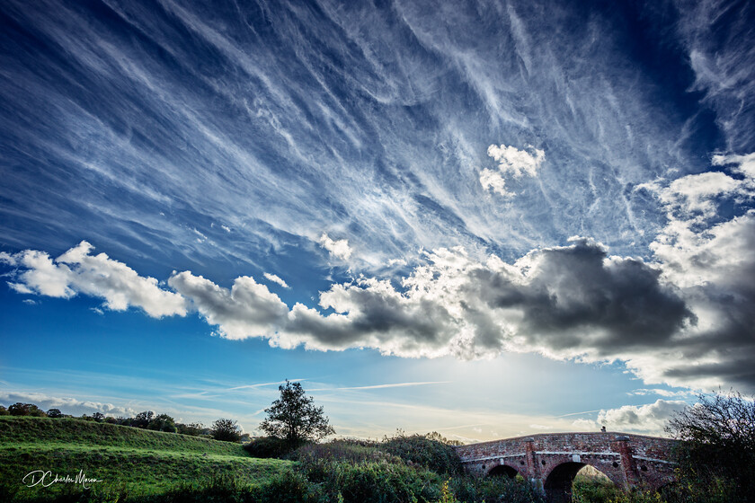 Bridge Over the Rother 
 Waiting on the outskirts of Bodiam castle with the camera on a tripod watching the clouds rise, fall, and change shape as the sun moves to eventually set behind the bridge that crosses the River Rother. 
 Keywords: River Rother, dramatic Sussex sky, bridge, Sussex landscape